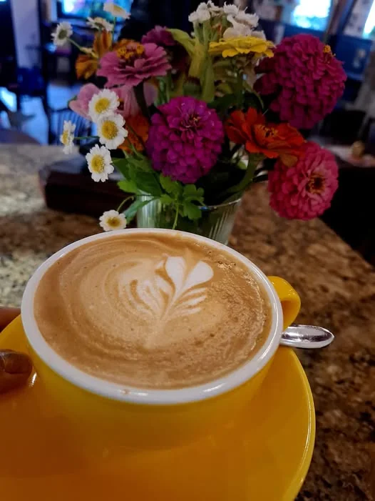 Latte art v žlutém šálku vedle kytice